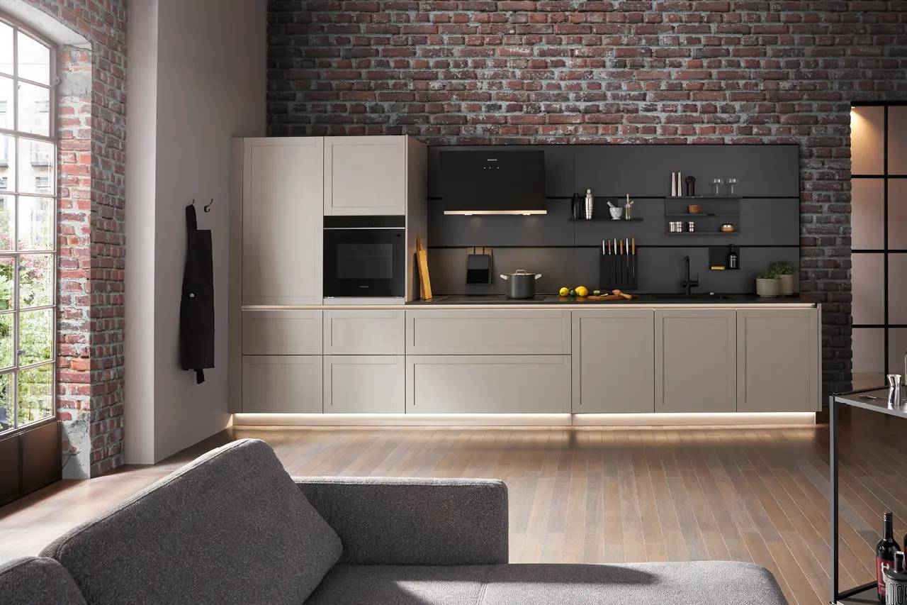 Moderne Einbauküche im Industrial Stil mit hellen Fronten, schwarzer Küchenrückwand, Backsteinwand und integrierten Elektrogeräten in offenem Wohnraum mit Holzboden